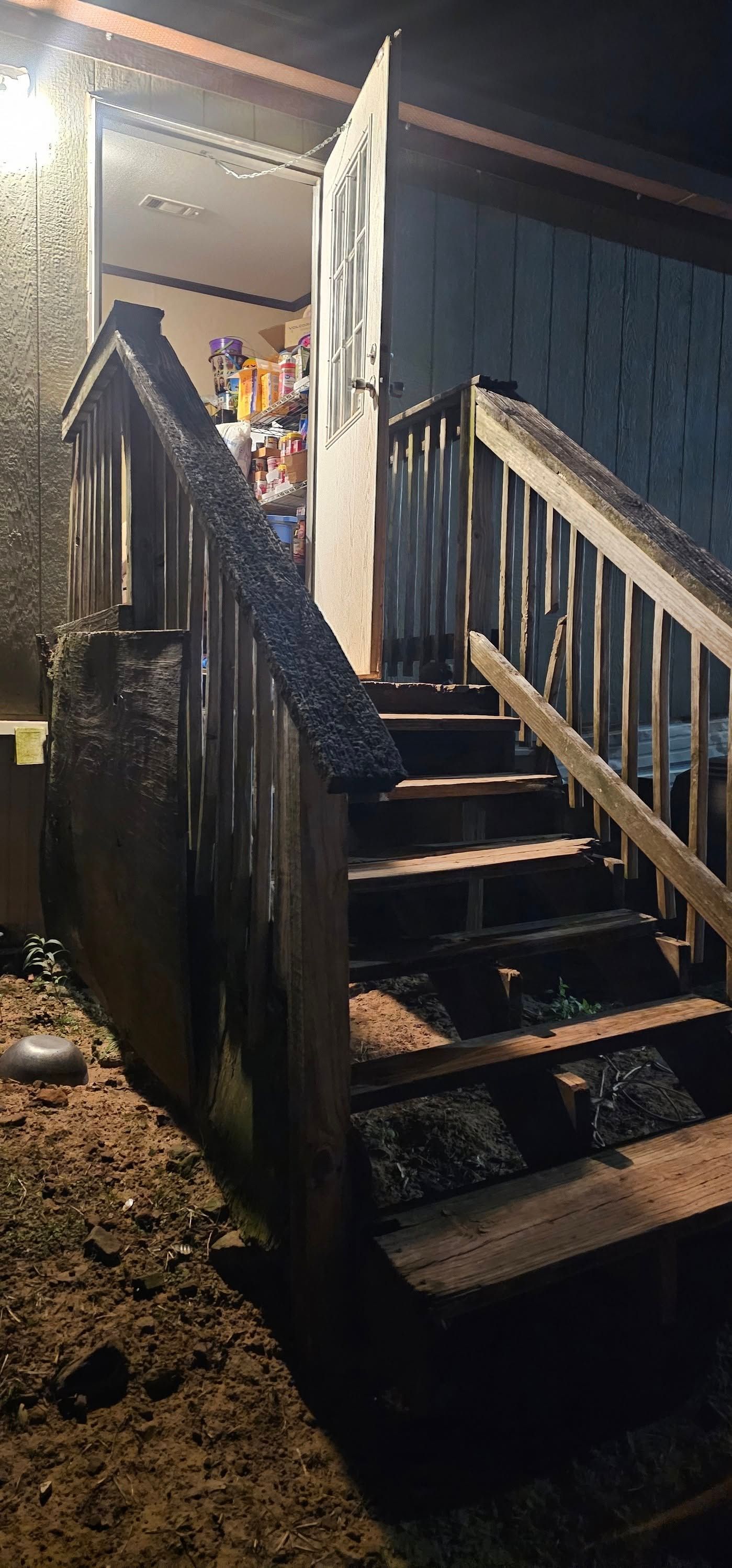 Rainy porch stairs with a lit doorway and wooden railings at night