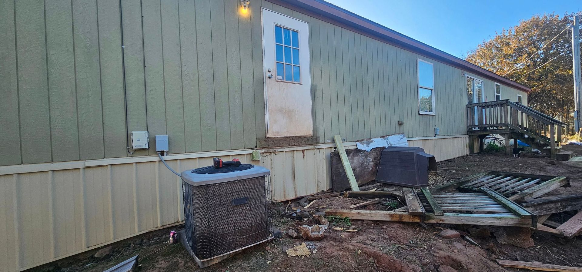 Damaged mobile home exterior with siding, broken skirting, debris, and a tilted roofline