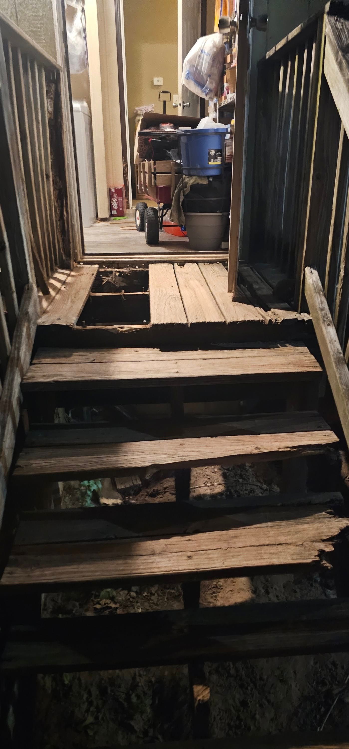 Narrow wooden stairway in a cramped alley, with a person at the top near a blue container.
