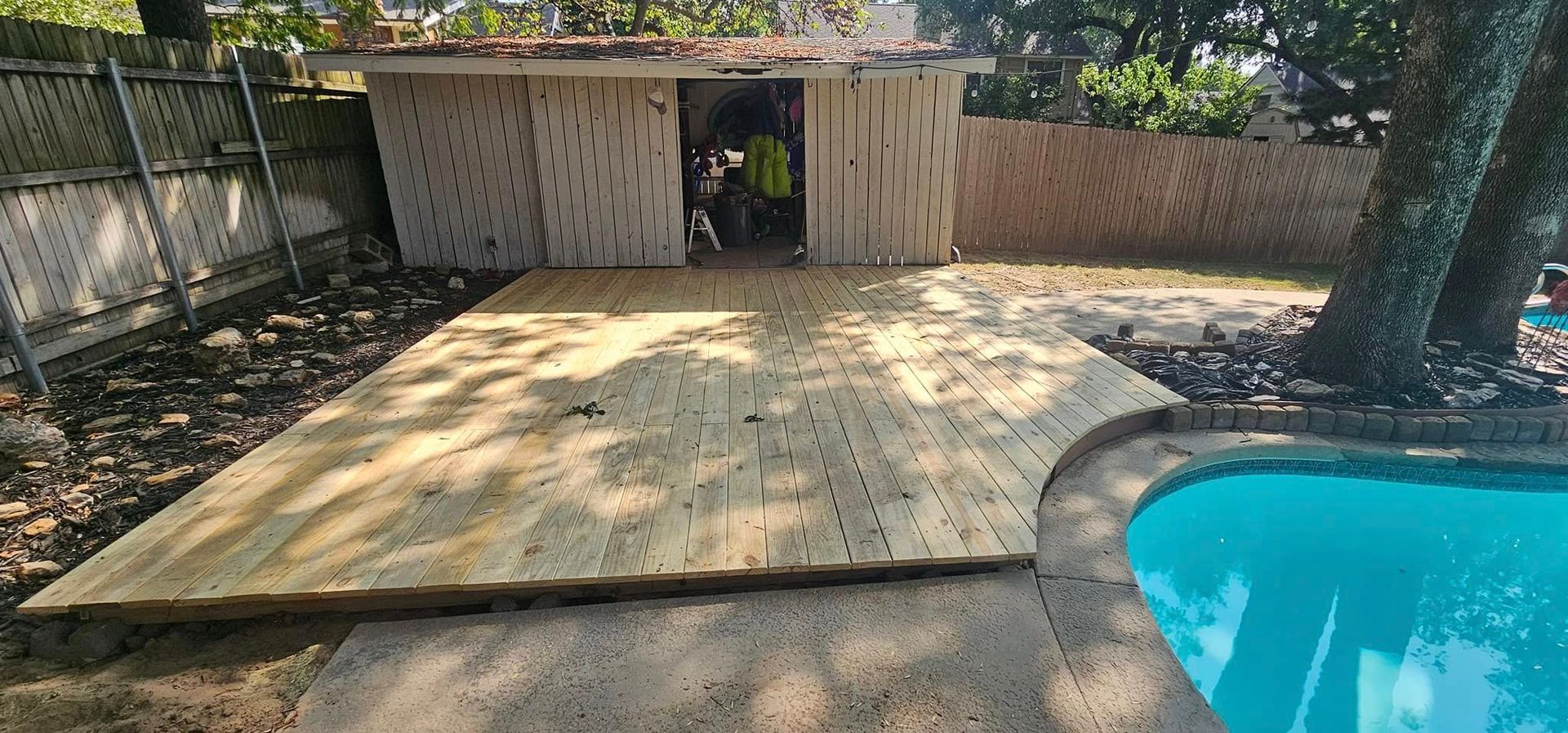 Backyard patio with a pool, concrete deck, and shed under trees