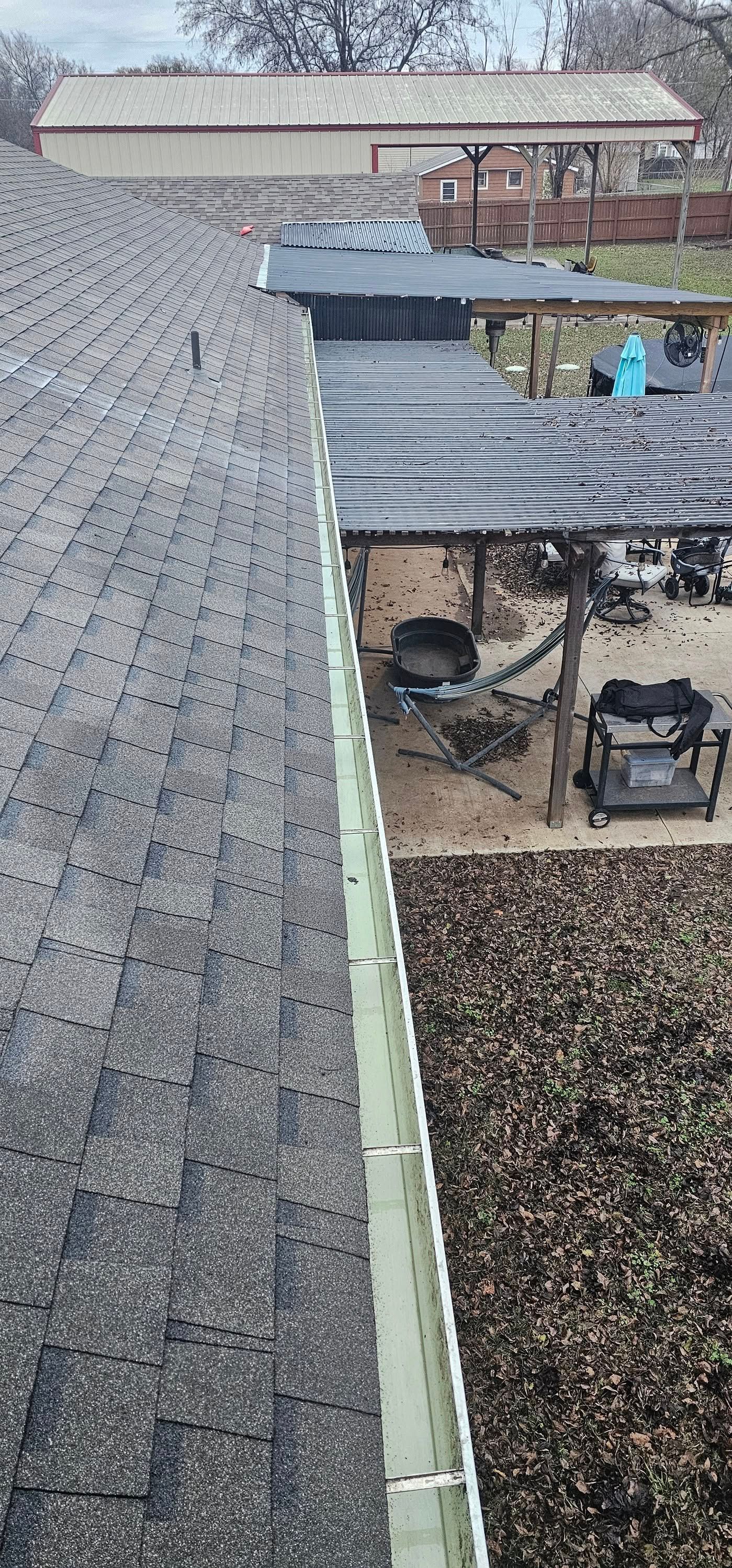 Snow-covered shingled rooftop beside a covered patio with outdoor furniture and a grill