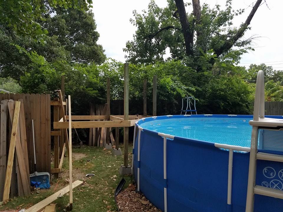 Backyard with blue above-ground pool, wooden deck, and trees beside a fence
