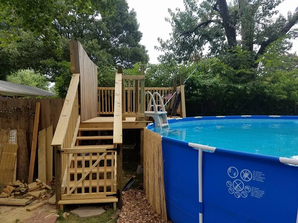 Wooden pool deck under construction beside a blue above-ground pool, with trees in the background
