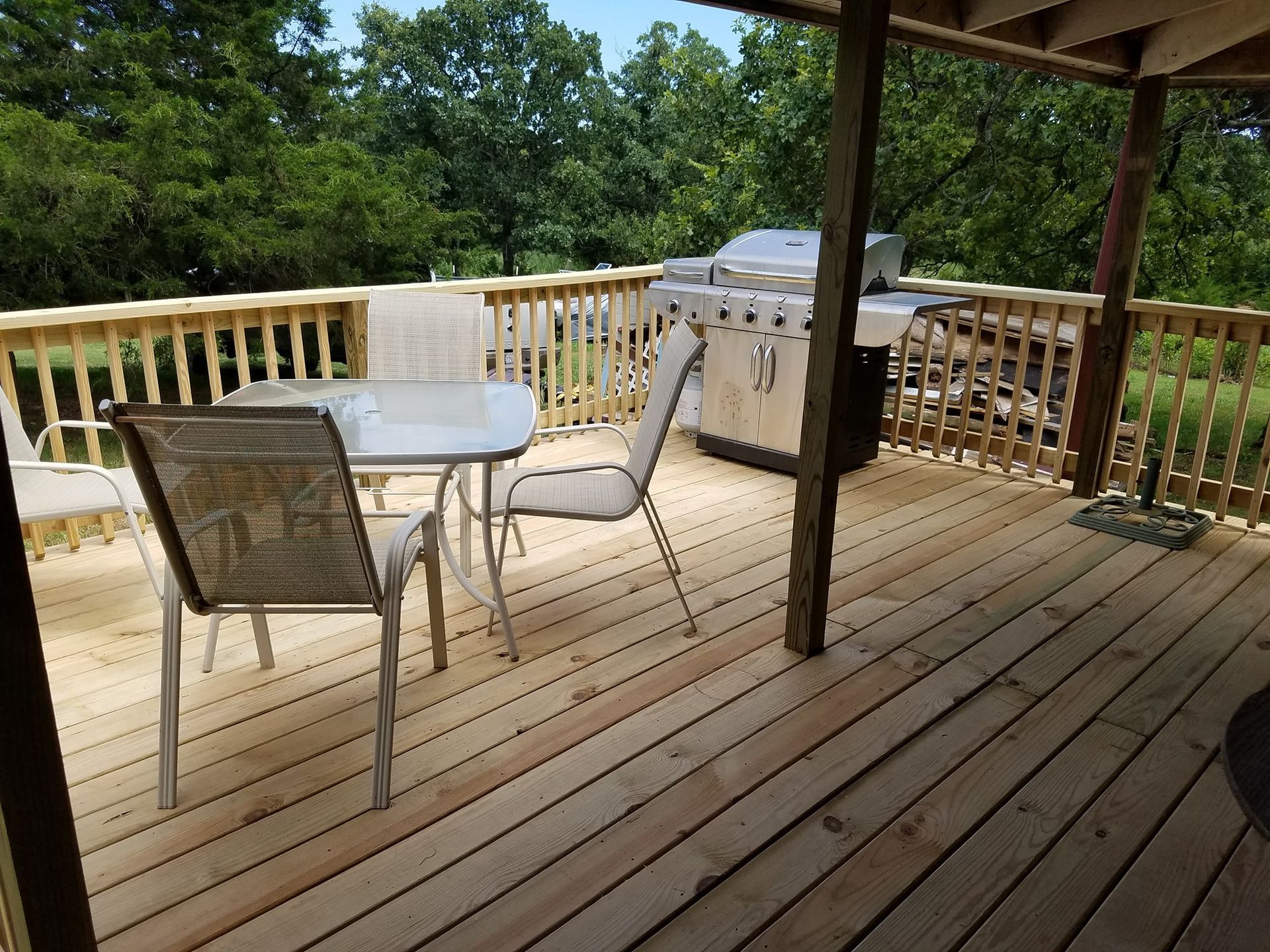 Wooden deck with patio table, chairs, and a grill overlooking trees.