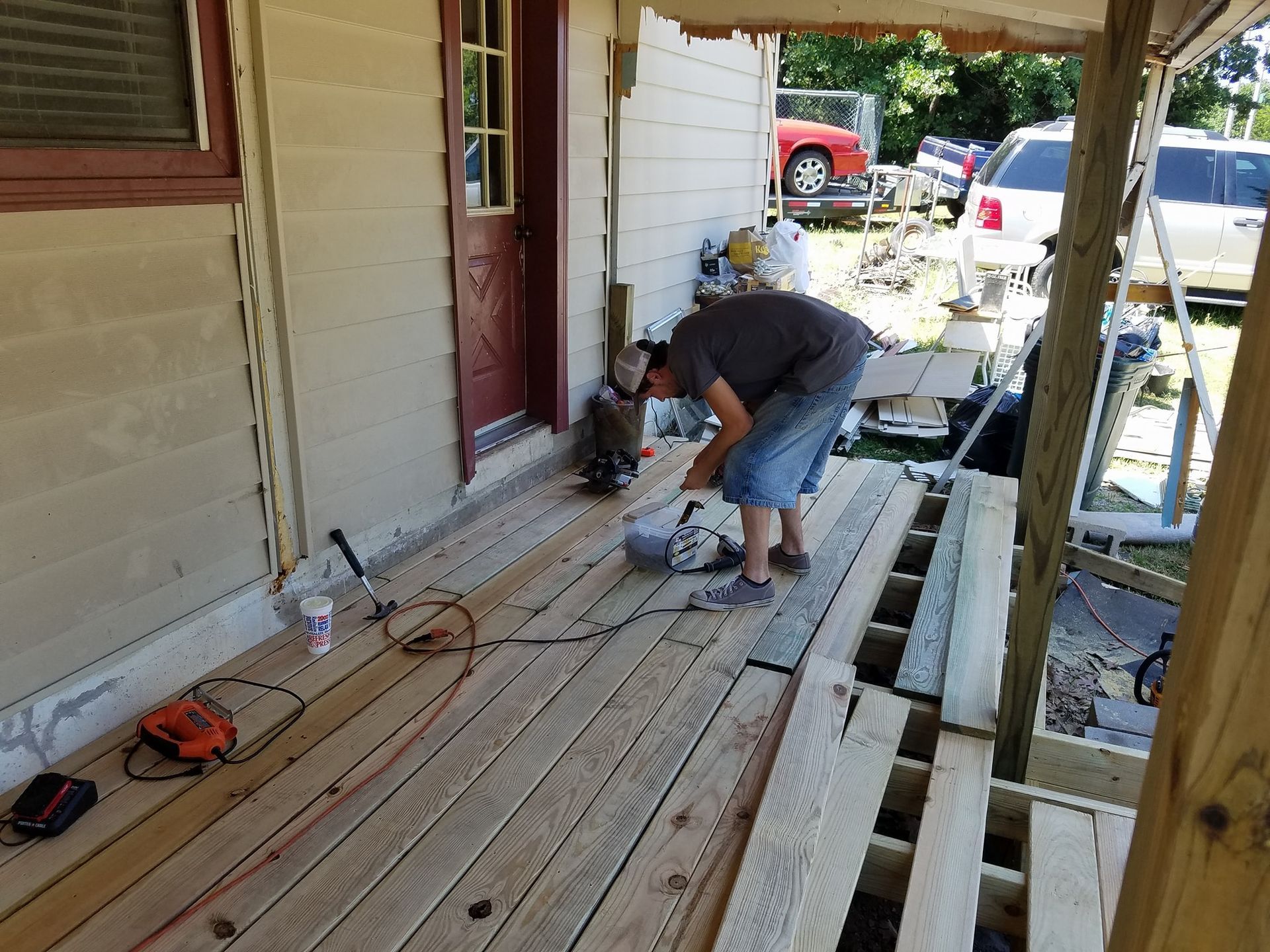Person working on a wooden porch deck with power tools and lumber during ремонта