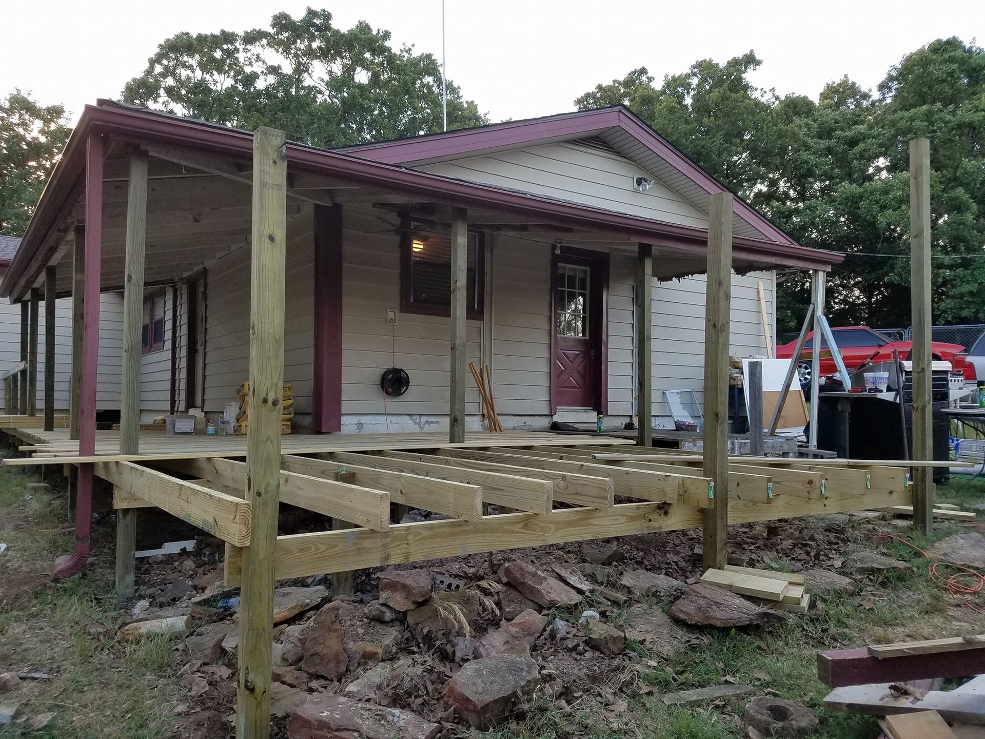 Raised porch under construction on a small house with wooden posts and unfinished deck framing.
