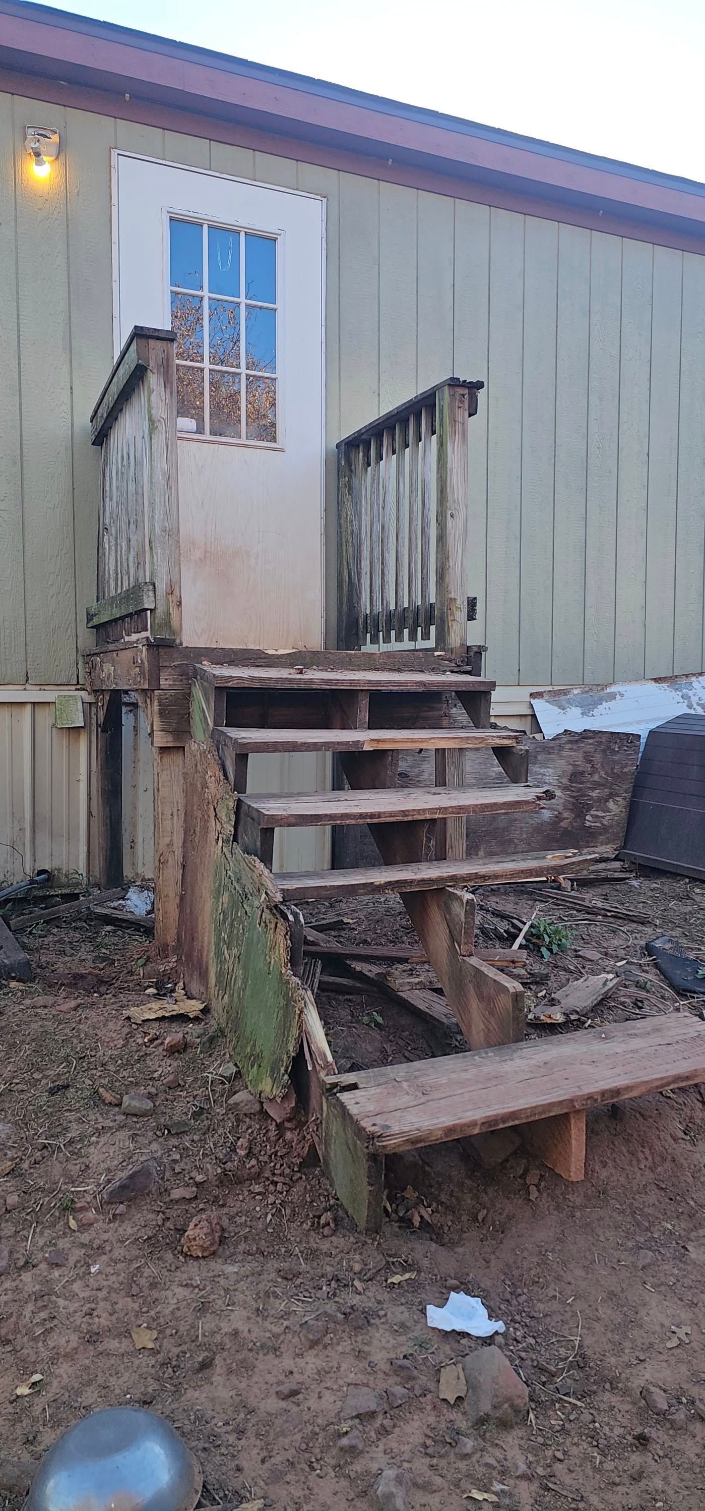 Weathered wooden steps leading to a side door on a beige house in a muddy yard