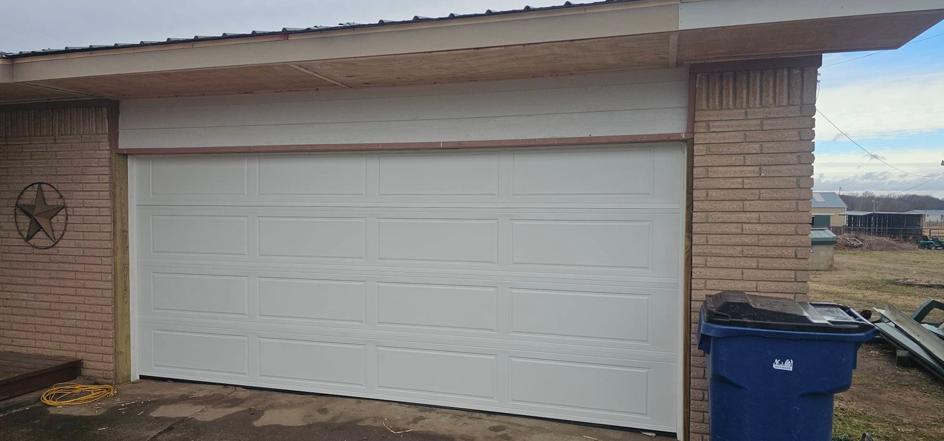 White garage door on a brick house exterior with a blue recycling bin nearby.