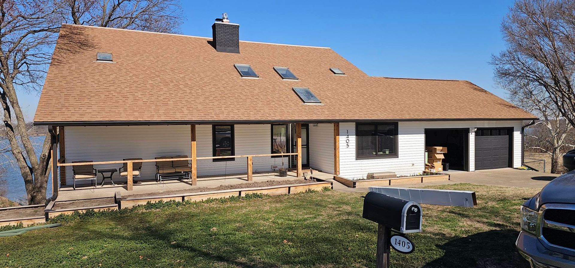 Suburban house with tan roof, covered porch, garage, and lawn under a clear blue sky