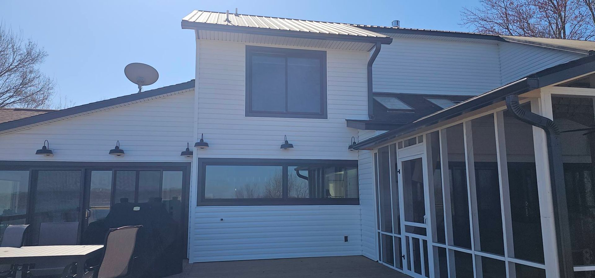 White two-story house exterior with screened porch, large windows, and a satellite dish on the roof.