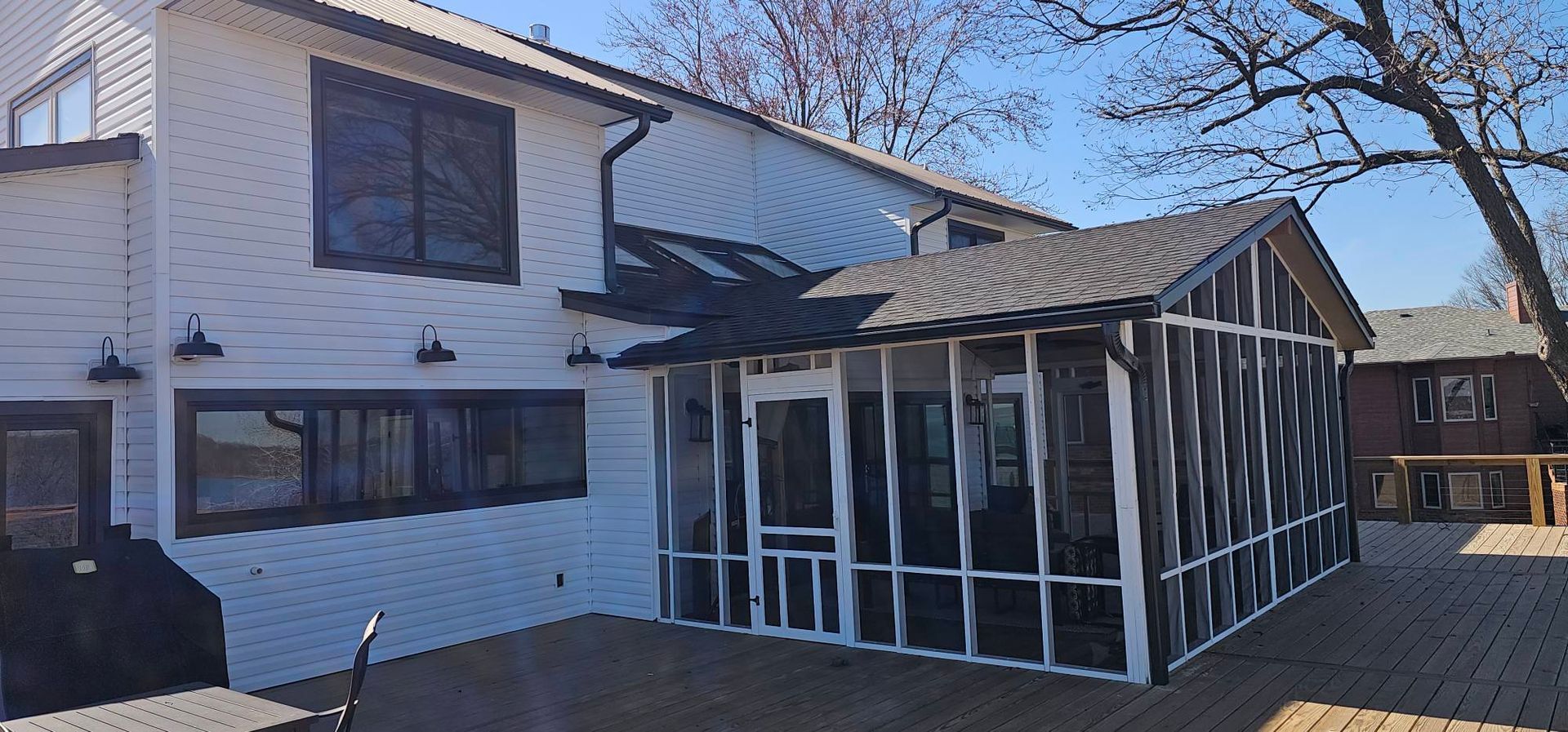 White two-story house with a screened porch and wooden deck under a clear blue sky