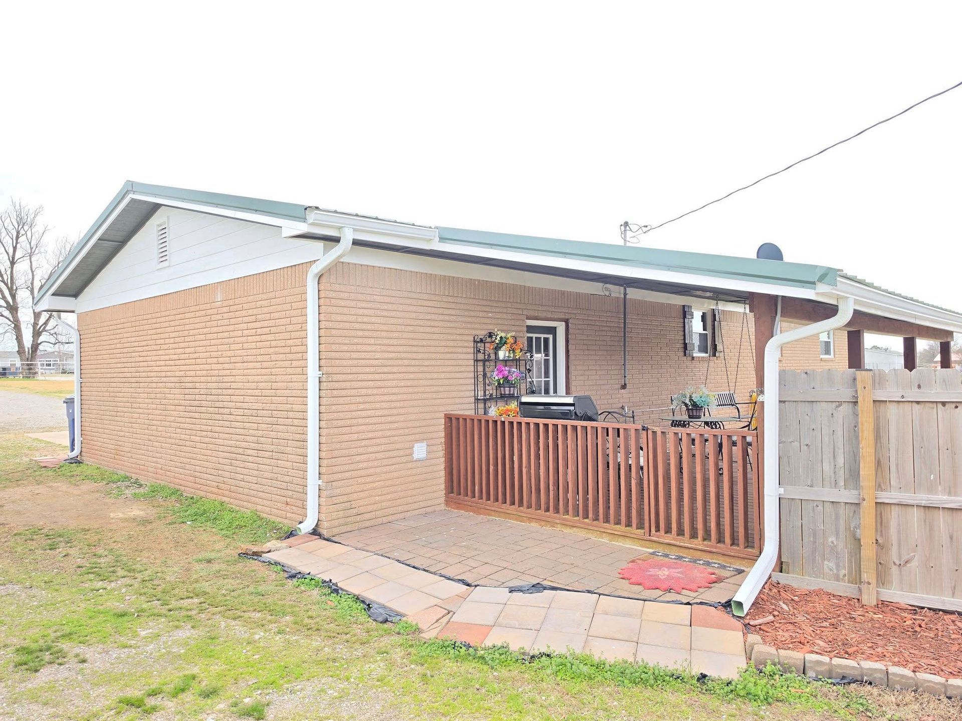 Brick house side yard with small fenced patio, white trim, and potted flowers