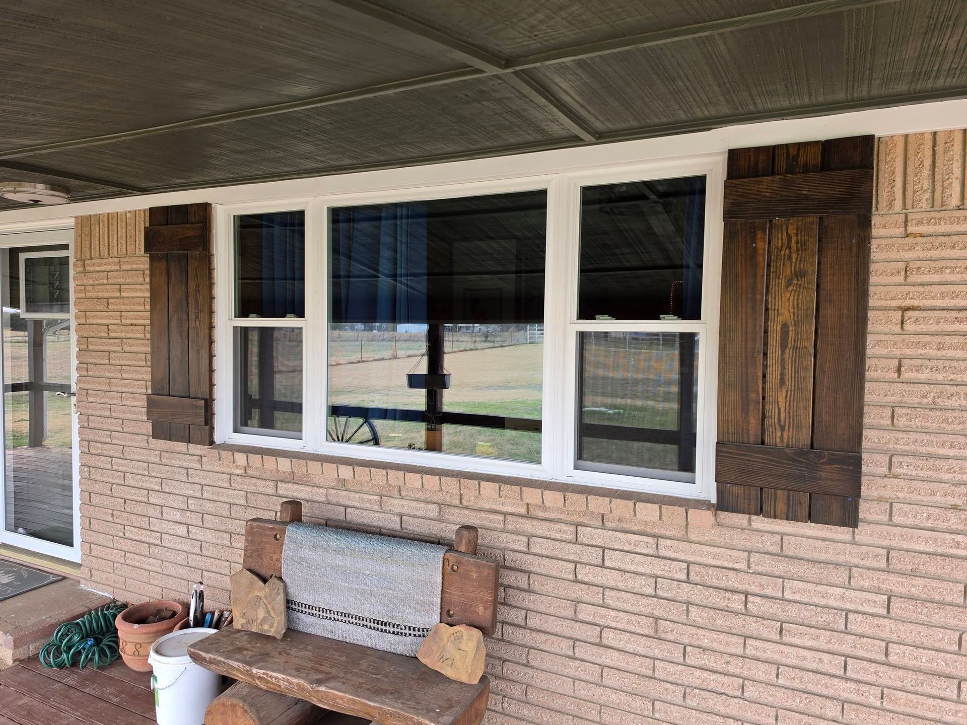 Brick house porch with white-framed windows, brown shutters, and a bench under the overhang