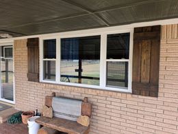 Brick house porch with white-framed windows, brown shutters, and a bench under the overhang