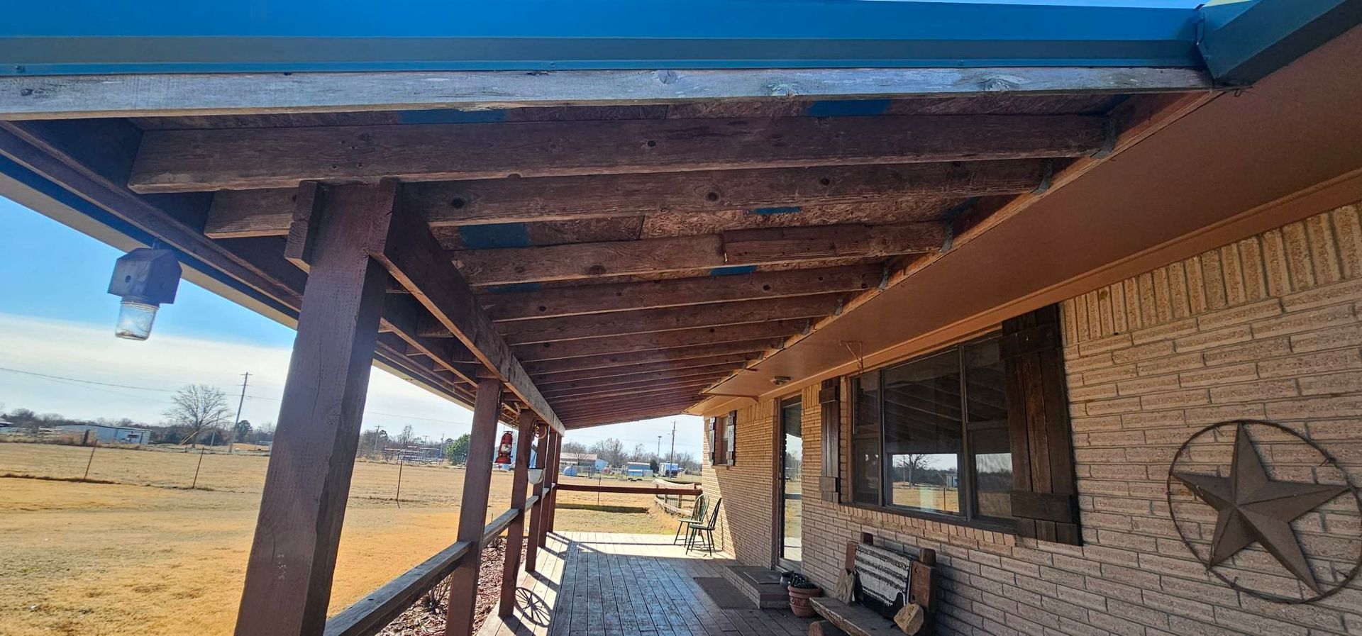 Covered porch walkway beside a brick house, with wooden posts and a star decoration on the wall.