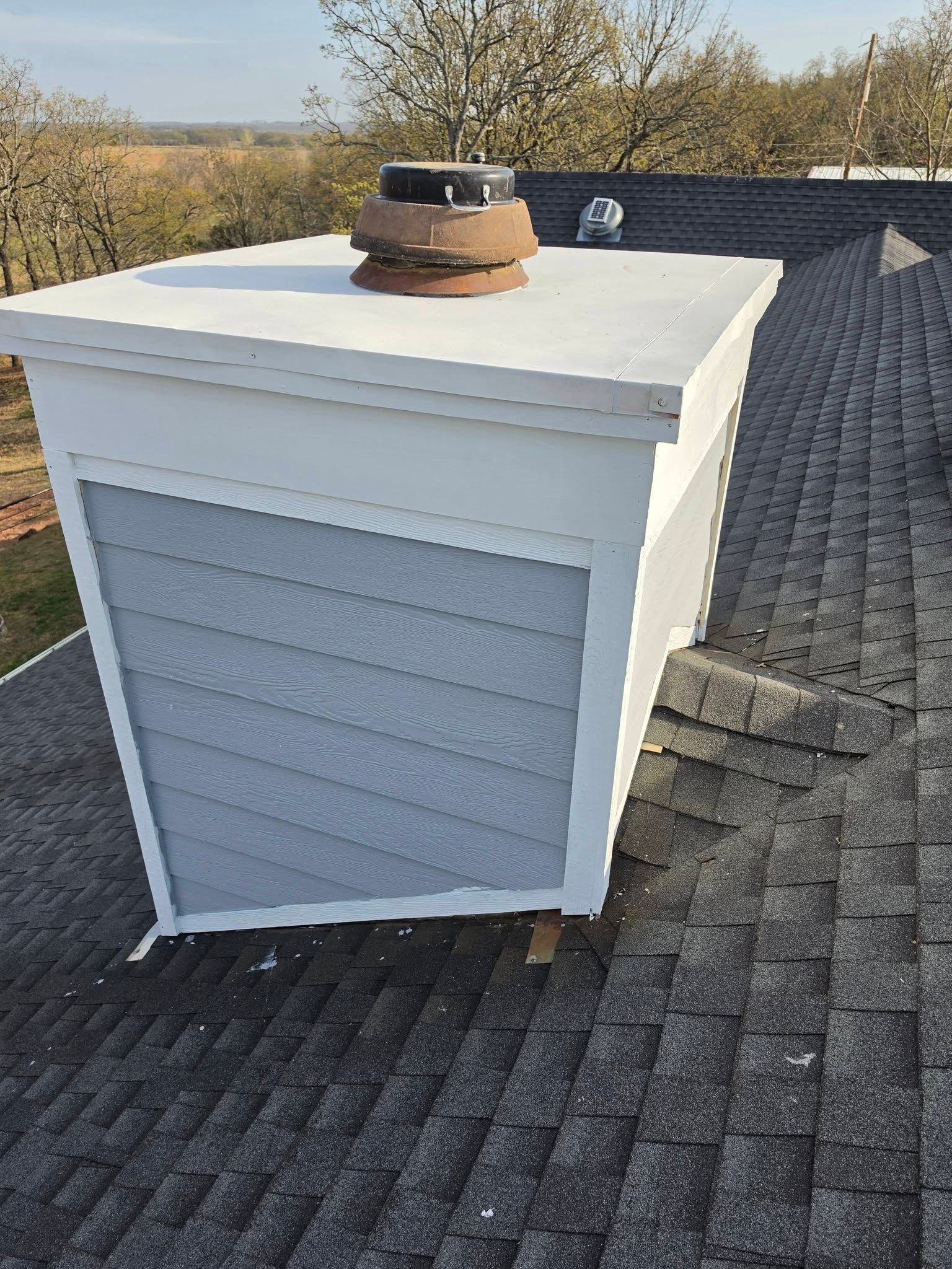 White rooftop vent on shingled roof with a brick chimney cap nearby under a clear sky