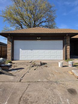 Brick house with a white garage door, concrete driveway, and construction debris in front.