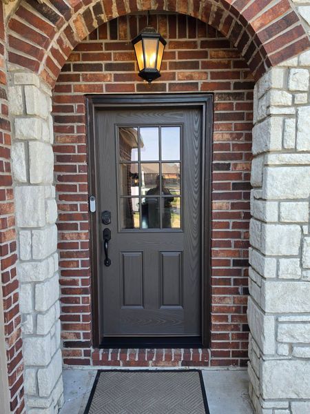Front entrance with dark gray door, brick archway, stone columns, and lantern light above.