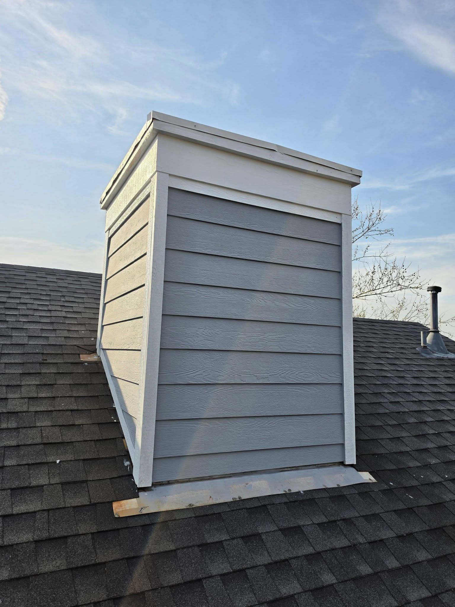 White dormer on a gray shingled roof under a blue sky