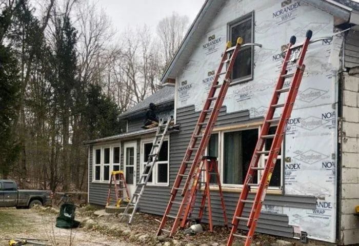 House under renovation with several ladders leaned against the siding and roof.