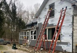 House under renovation with several ladders leaned against the siding and roof.