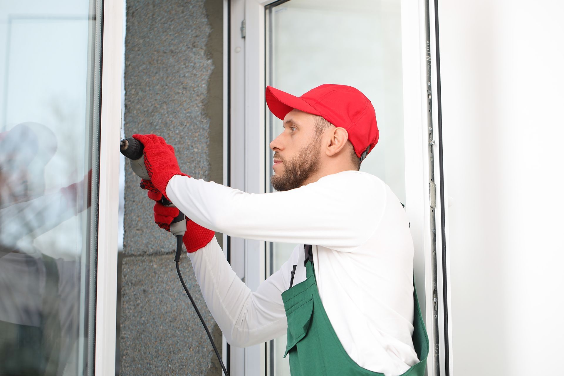 Worker in red cap and gloves installs exterior wall insulation beside a window