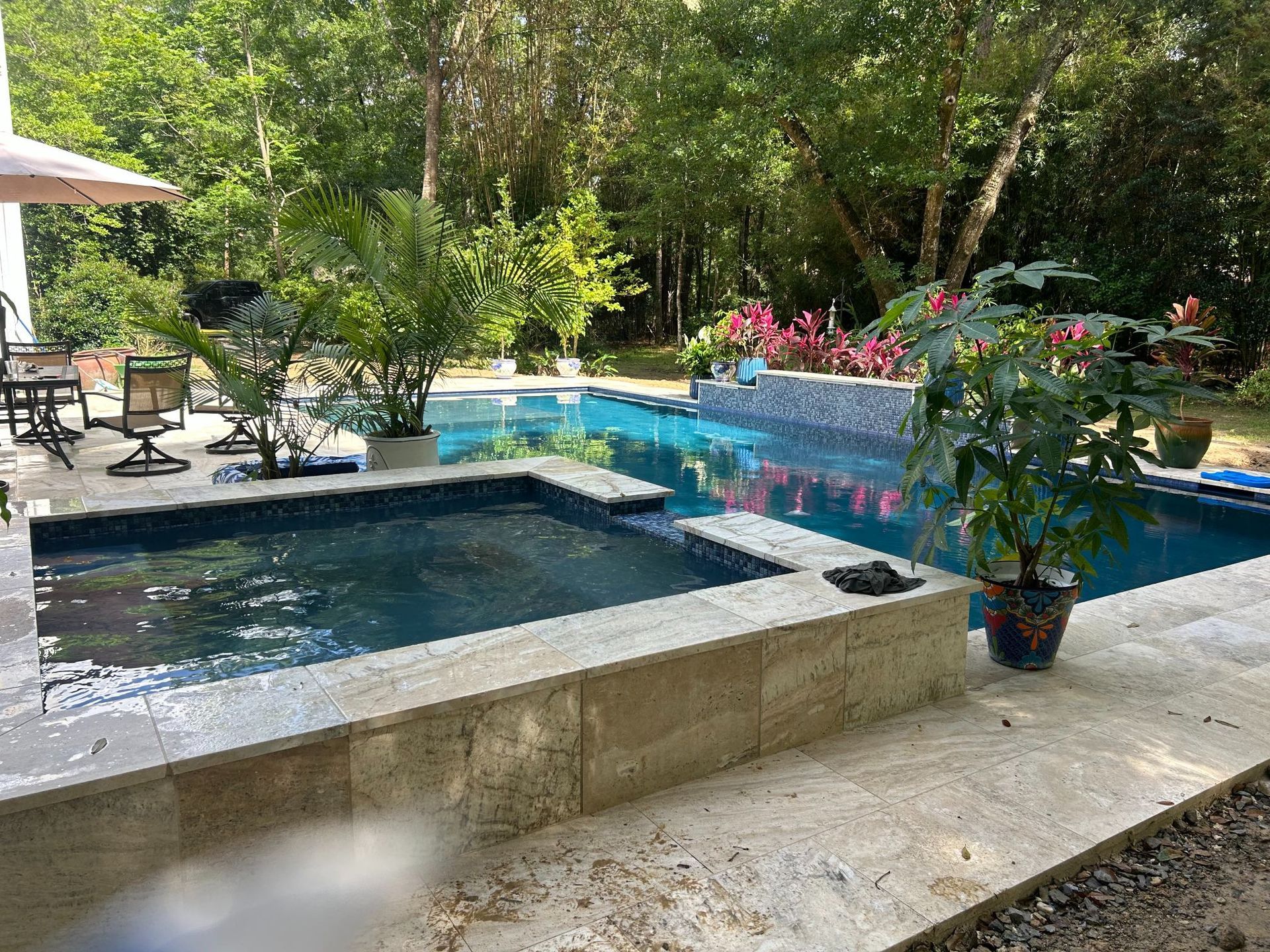 Backyard pool and hot tub with blue tile, surrounded by lush greenery and patio furniture