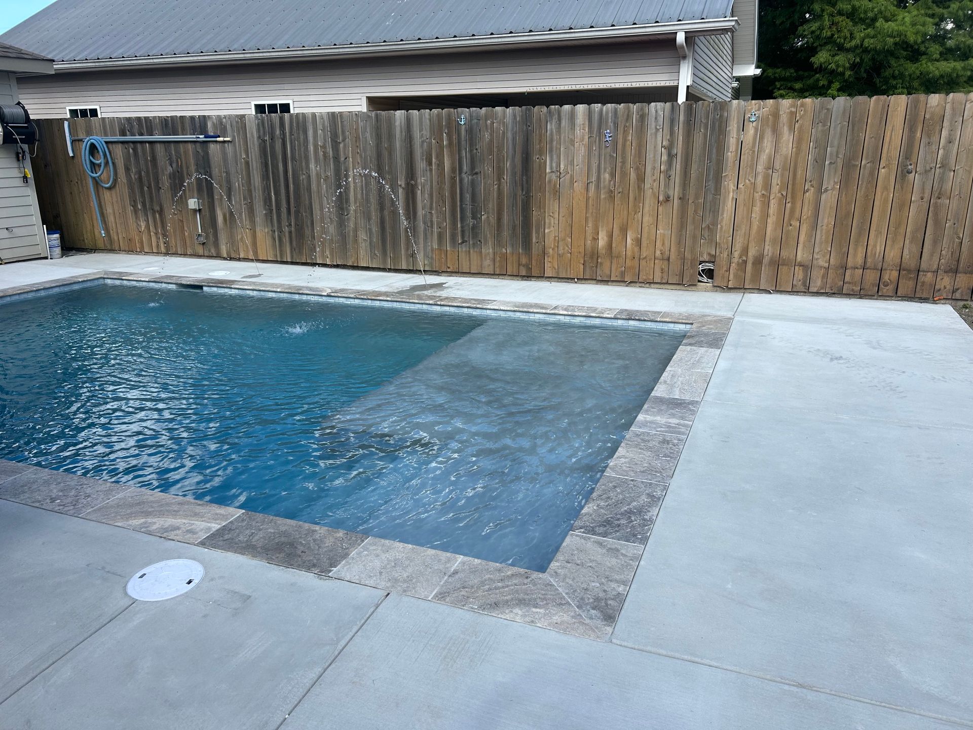 Backyard swimming pool with blue water, concrete deck, and wooden fence