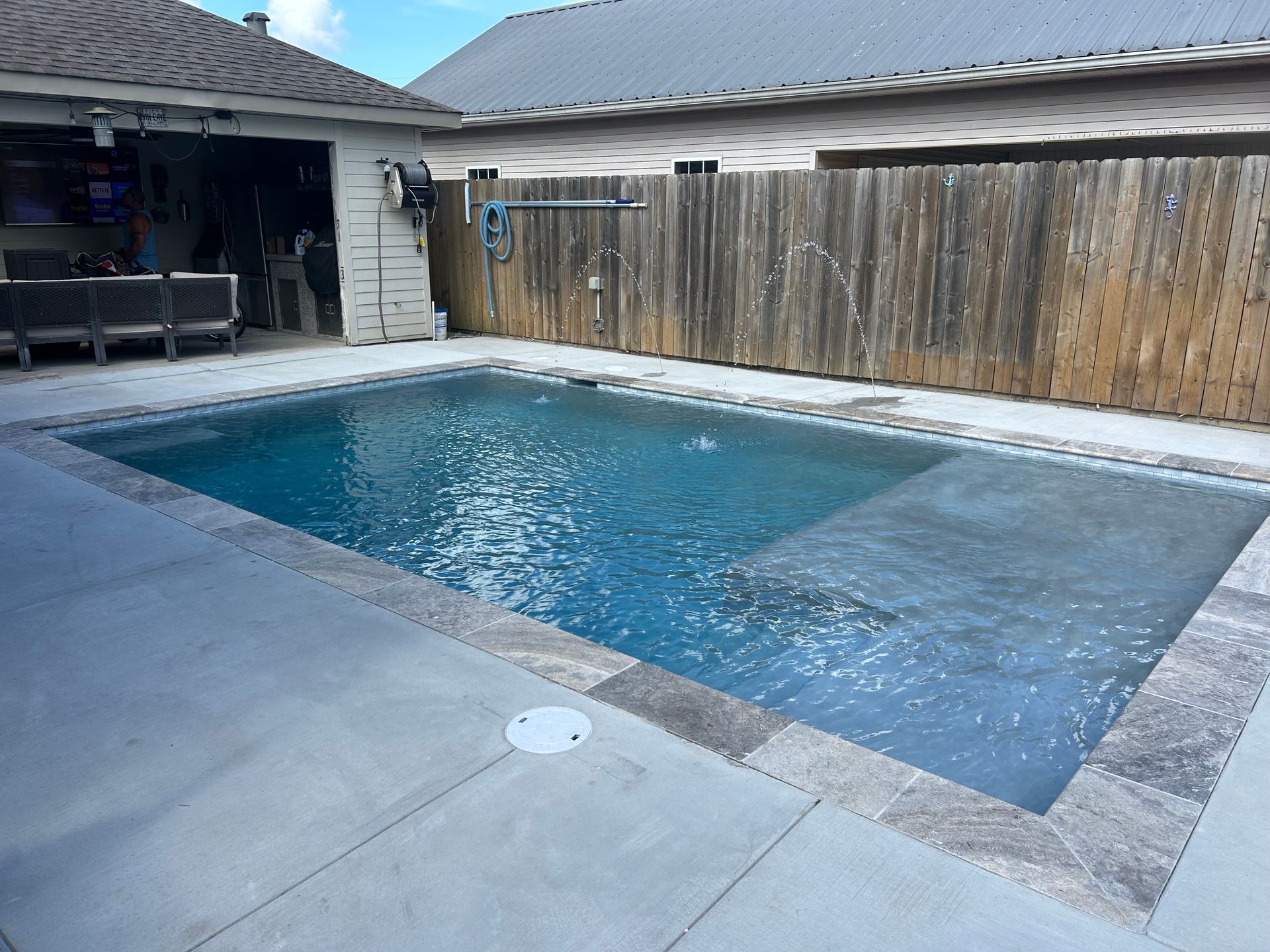 Backyard swimming pool with blue water beside a patio and wooden fence