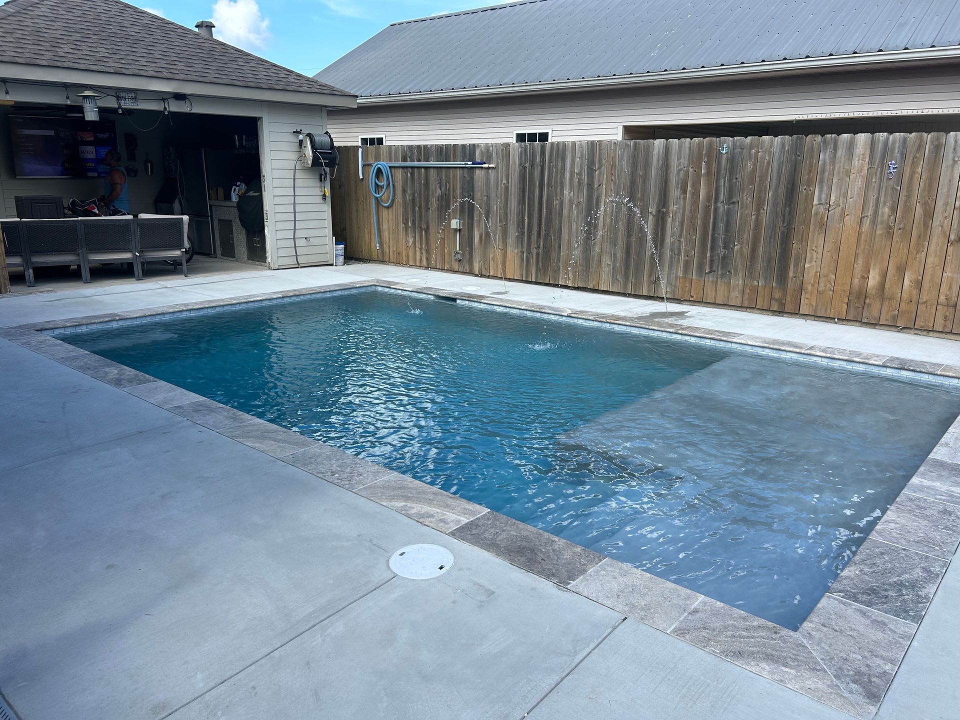 Backyard swimming pool beside a concrete patio and wooden fence