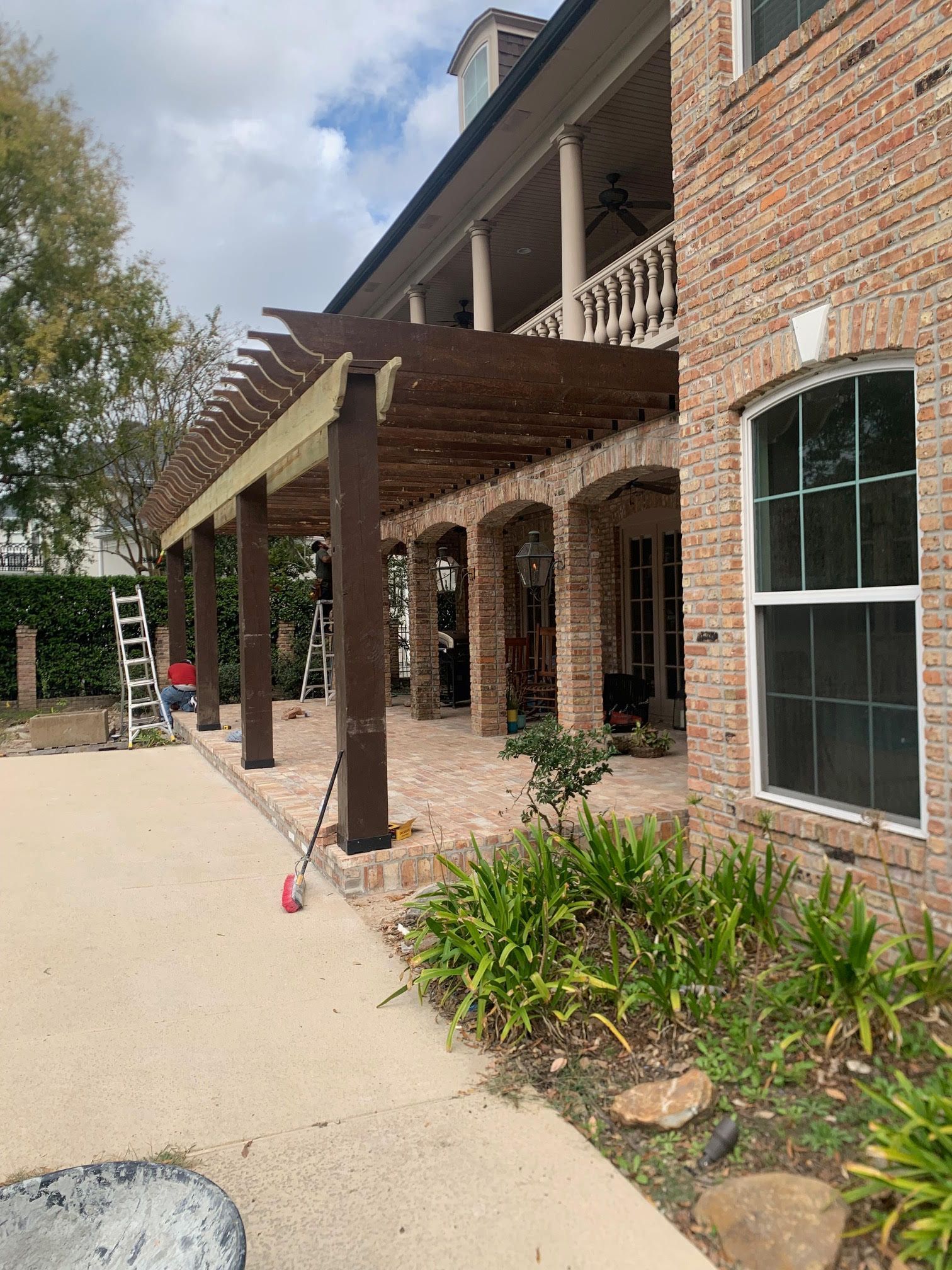 Brick house exterior with covered porch, windows, and a driveway with a ladder and garden plants