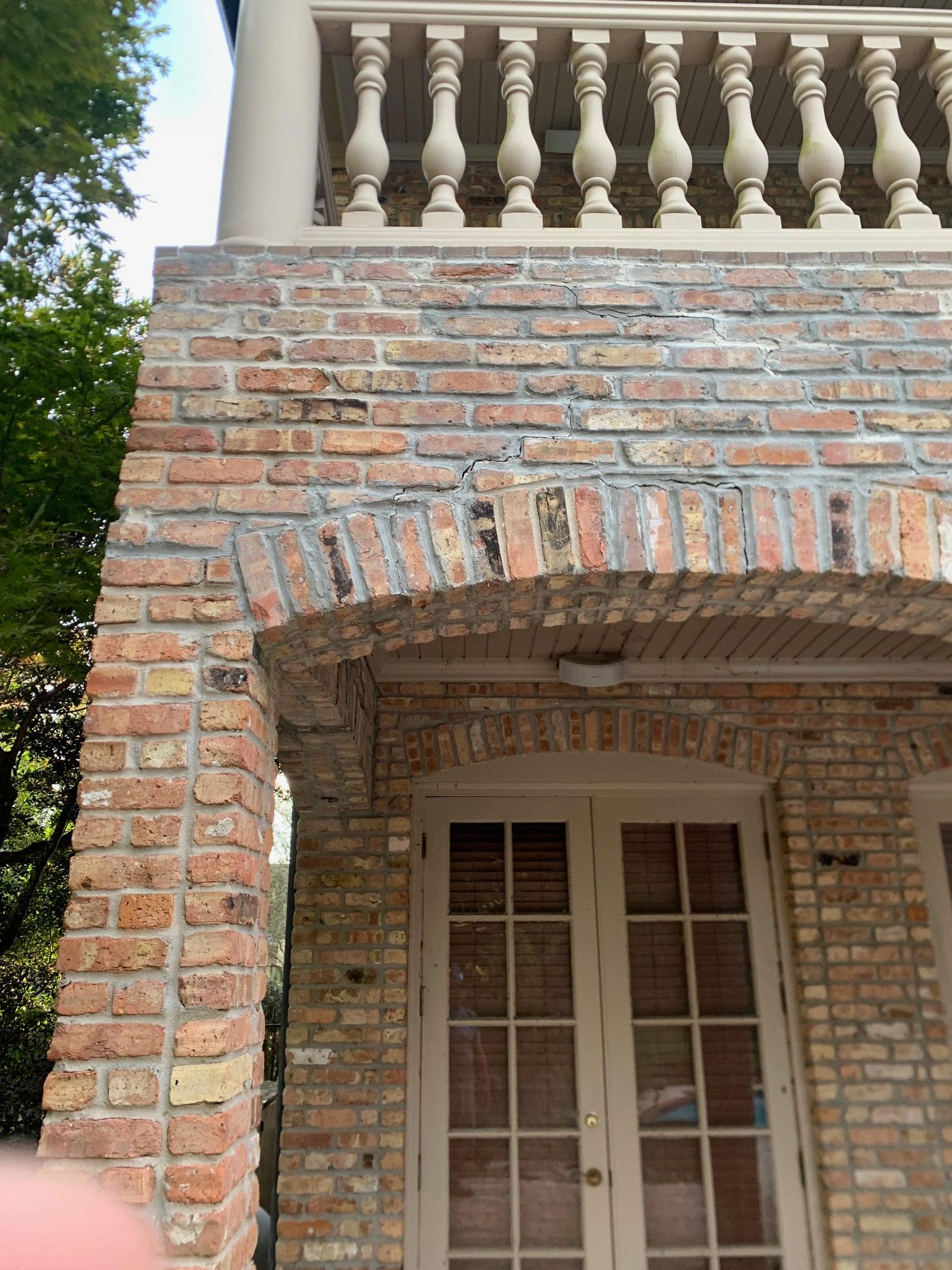 Brick house porch with arched entry, white balustrade above, and French doors beneath