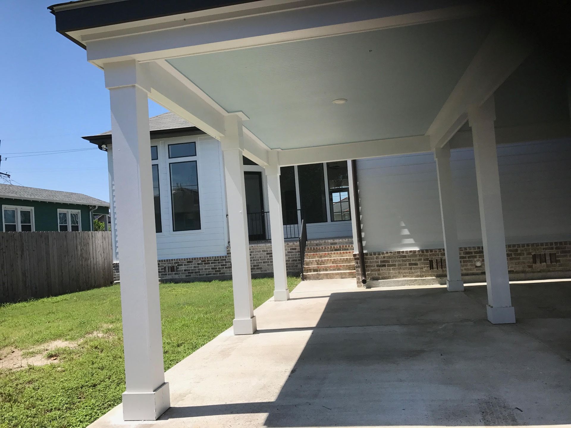 Covered concrete patio with white columns beside a house and grassy yard