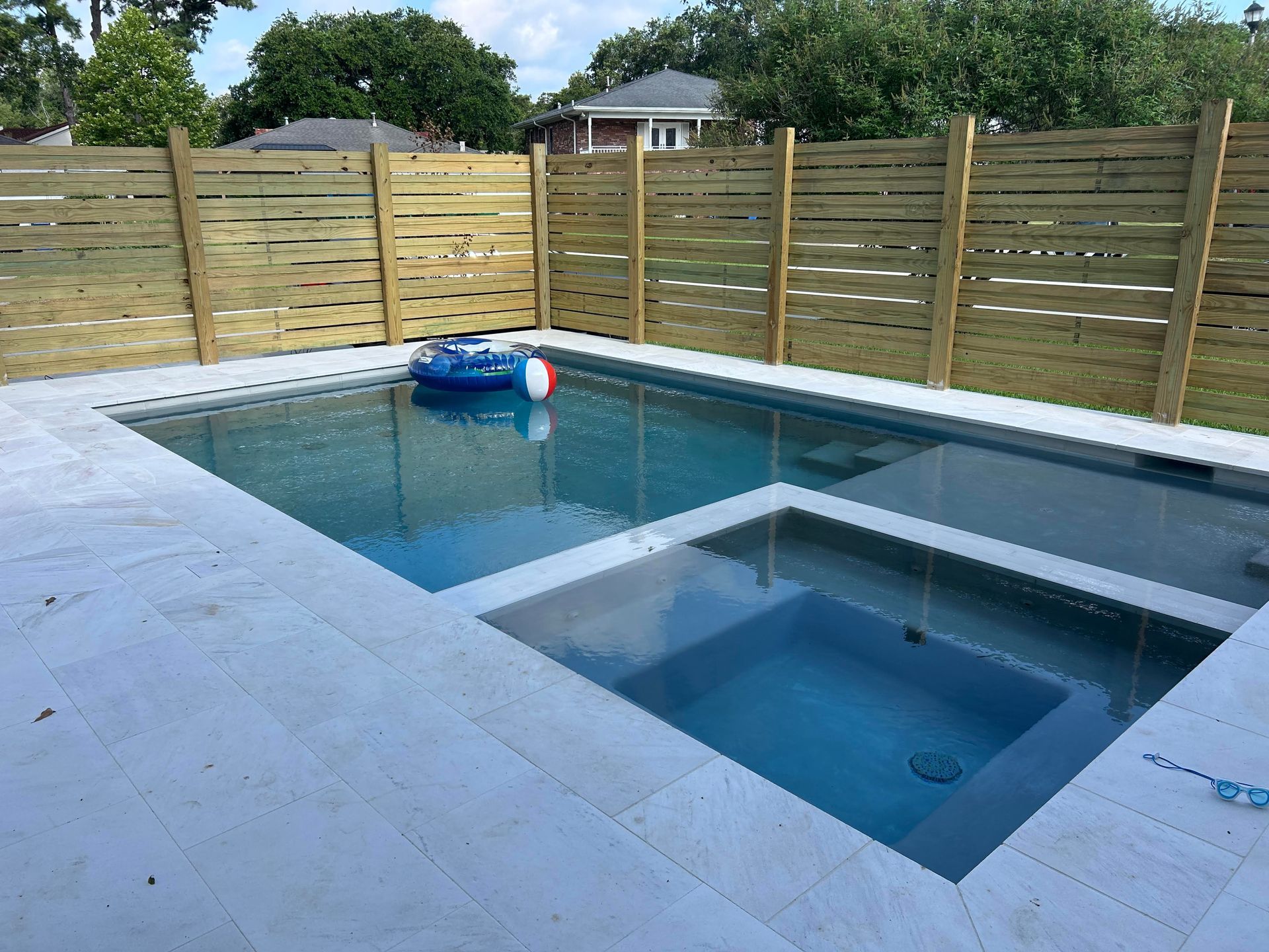 Backyard swimming pool with a raised spa, blue float, and wooden fence in the background