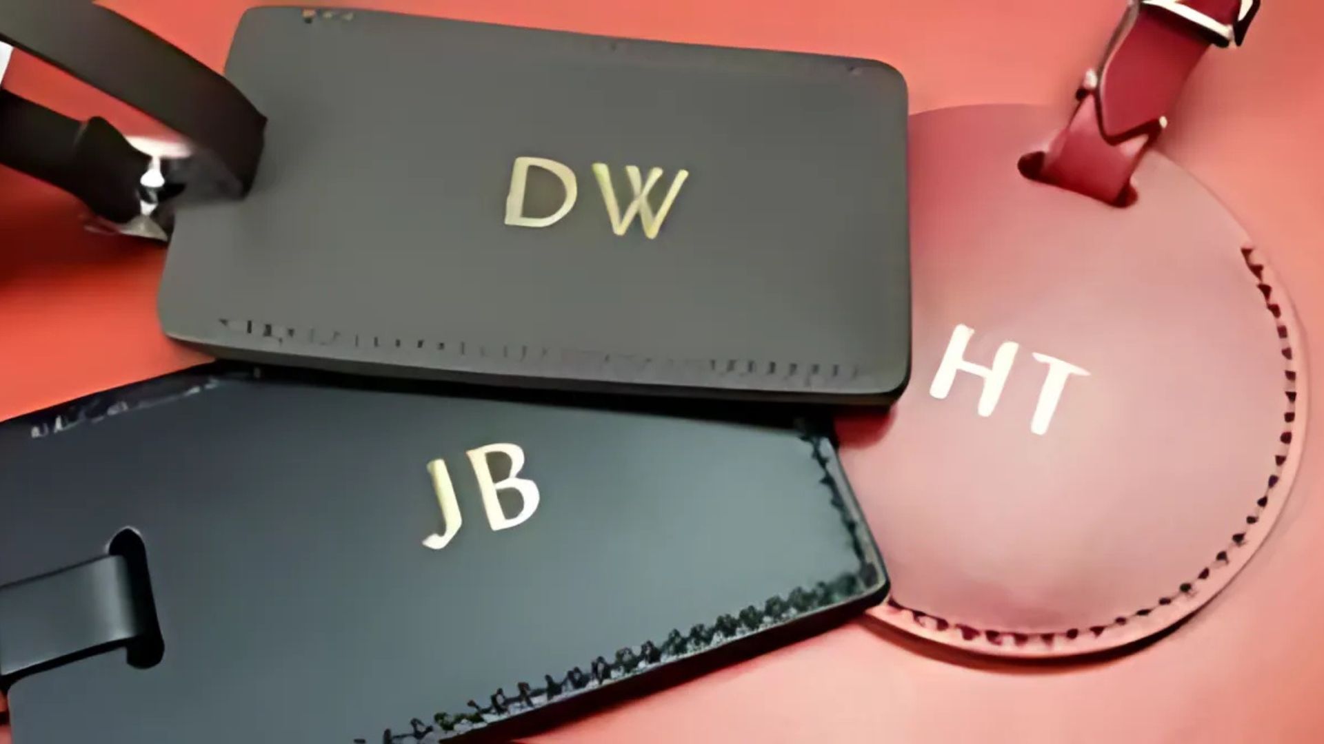 Three leather luggage tags: dark gray, black, and maroon. Each has initials in gold: DW, JB, and HT.
