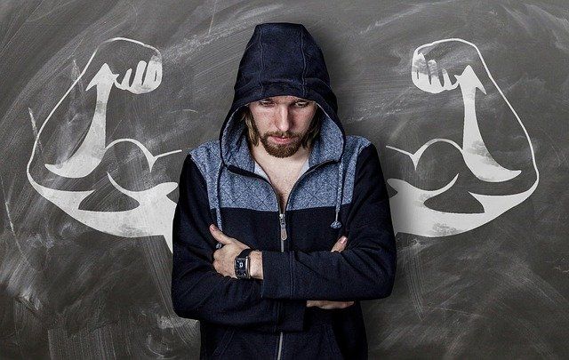 A man in a hoodie is standing in front of a blackboard with muscles drawn on it.