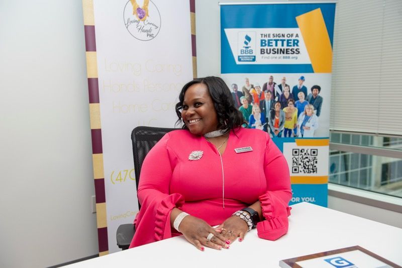 A woman in a pink dress is sitting at a table in front of a better business sign.