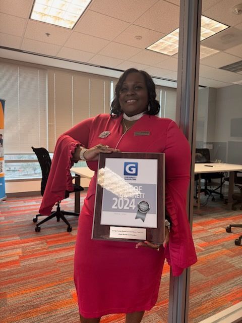 A woman in a pink dress is holding a certificate in an office.