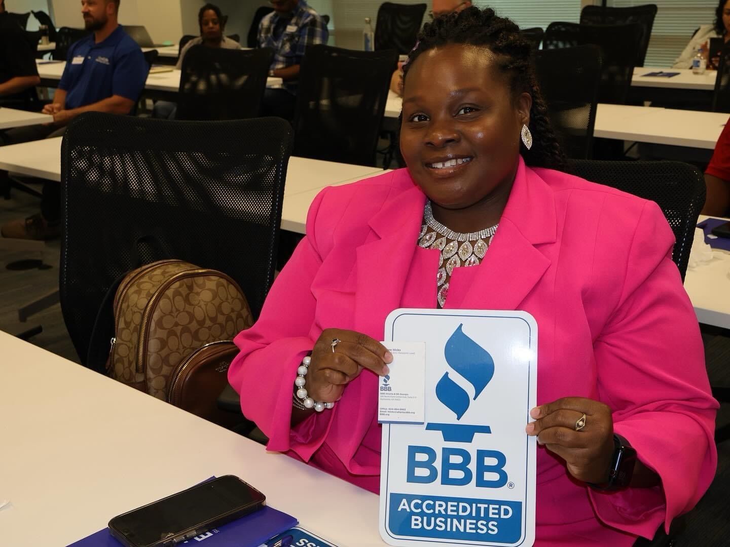 A woman in a pink jacket is holding a sign that says bbb accredited business