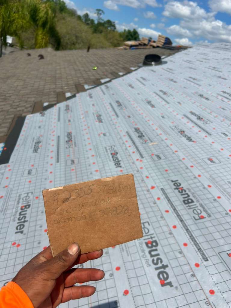 Hand holding a cork square over a rooftop underlayment with trees and blue sky in the background