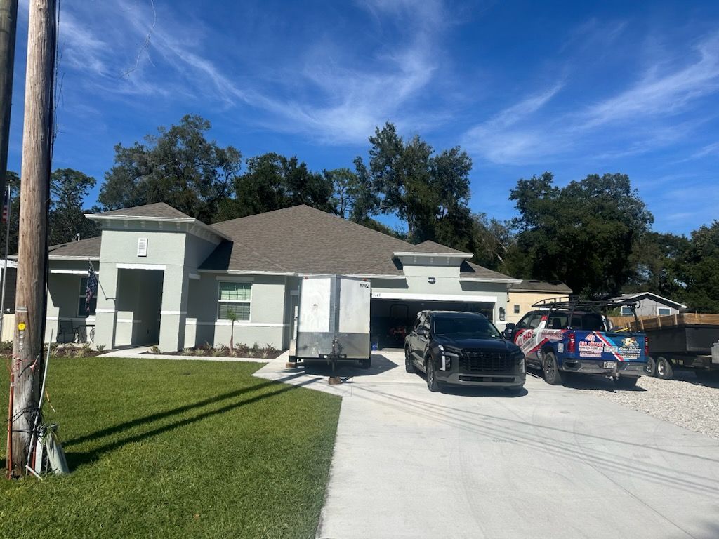 Single-story white house with a driveway, two parked vehicles, and a green lawn under a blue sky