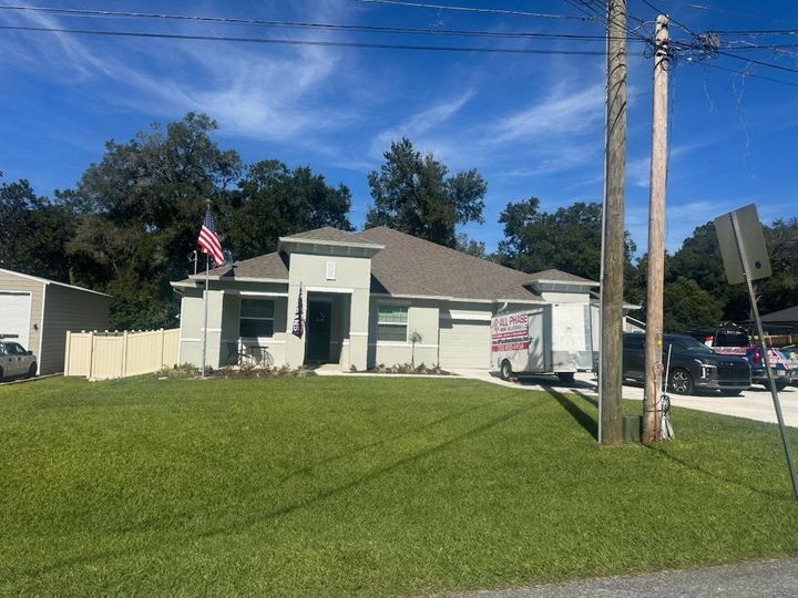 Small gray building with a U.S. flag, grassy lawn, and utility poles on a sunny street corner