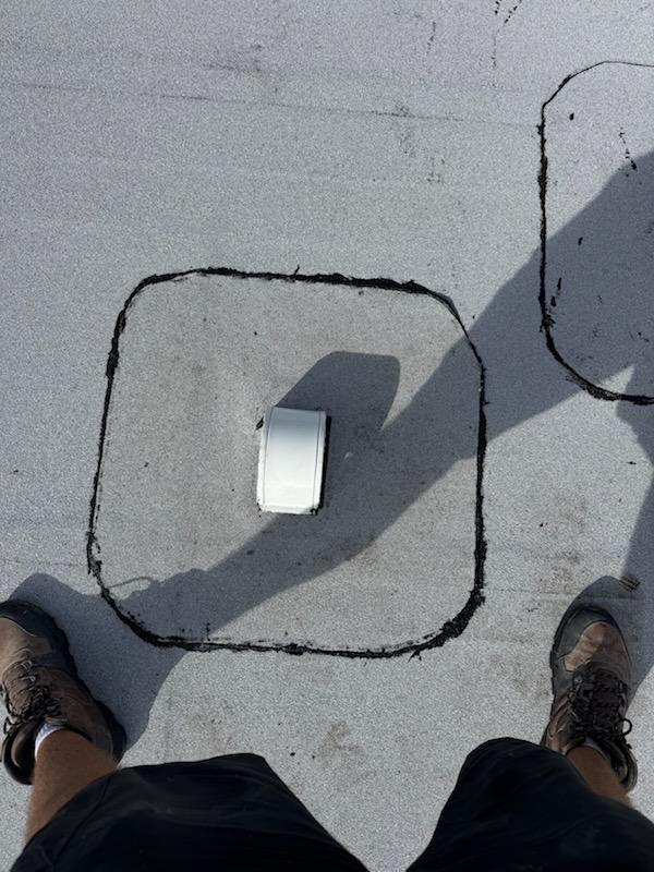 Top-down view of a white object on a gray sidewalk, outlined in black, with two shoes visible at the bottom.