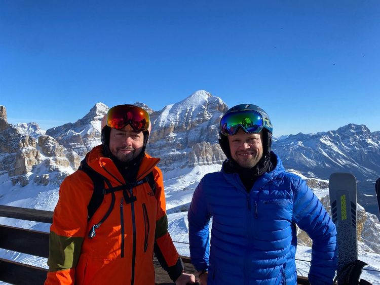 Two skiers in red and blue jackets posing in snowy mountains with skis beside them