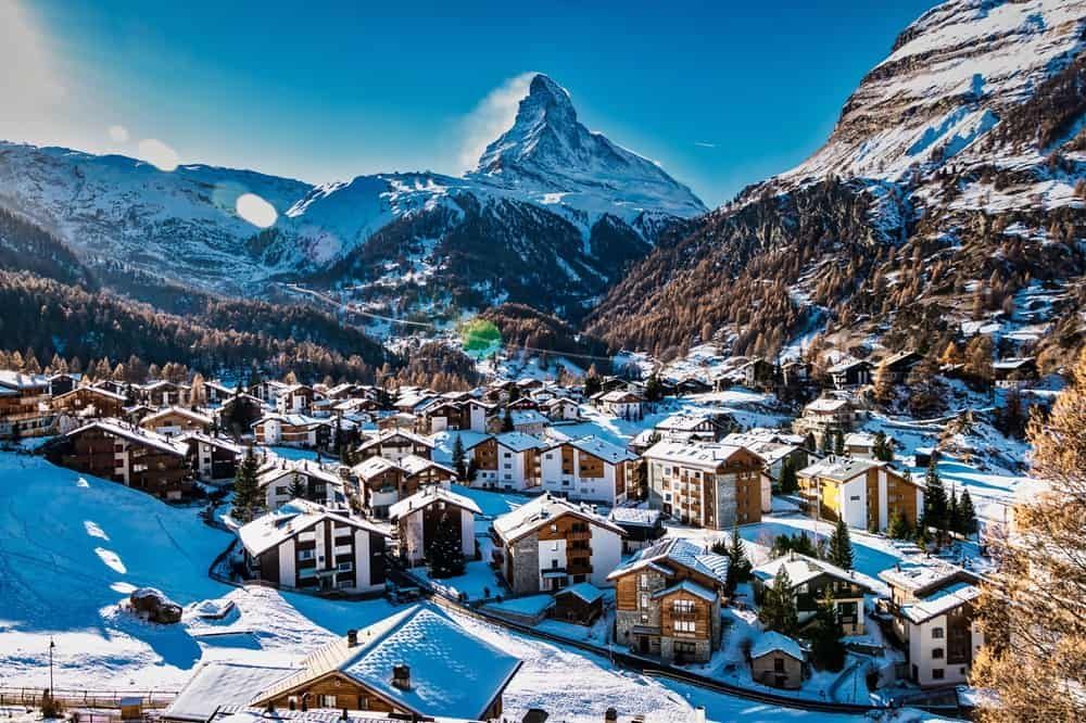 Snowy alpine village beneath a sharp mountain peak under a clear blue sky