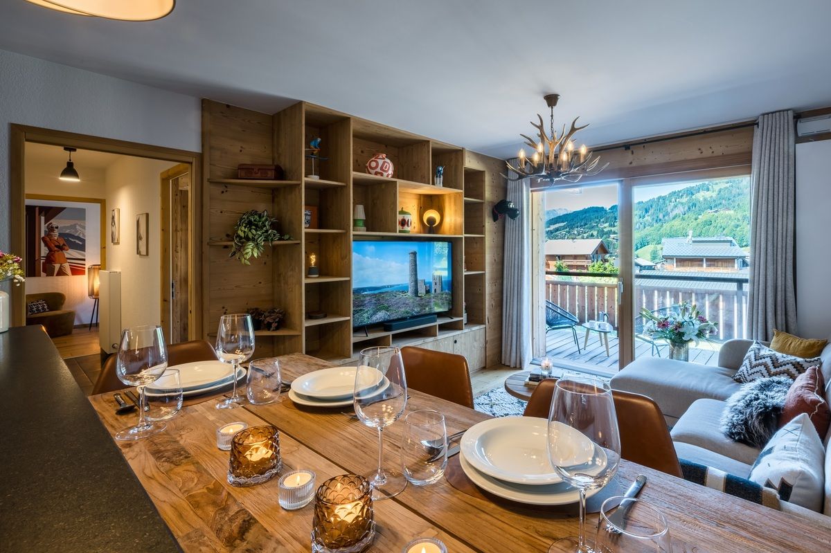 Modern dining and living room with wooden table, TV wall, sofa, and balcony view