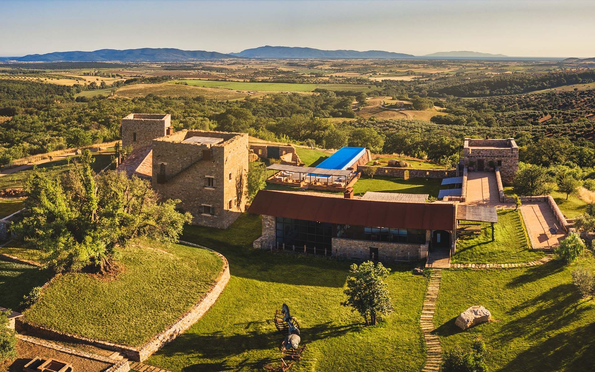 Rural stone estate with a blue-roofed pool, green lawn, and rolling hills in the distance