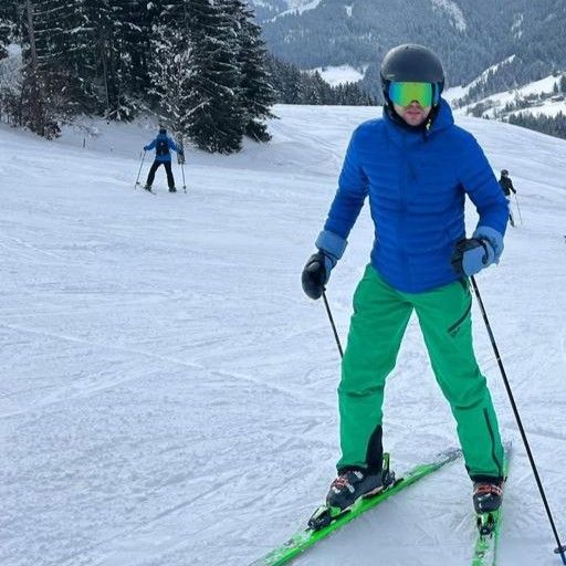 Skier in blue jacket and green pants skiing downhill on a snowy mountain slope