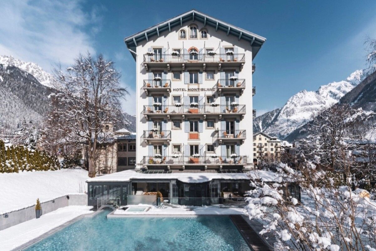 Snowy alpine hotel with a pool, framed by mountains and a clear blue sky
