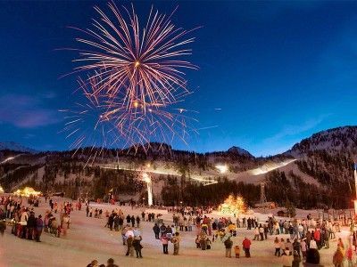 Fireworks over a snowy mountain crowd at dusk with people gathered on the slope